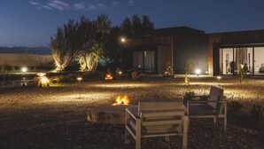 Un entorno moderno al aire libre con una fogata, zona de estar y un edificio con grandes ventanales.