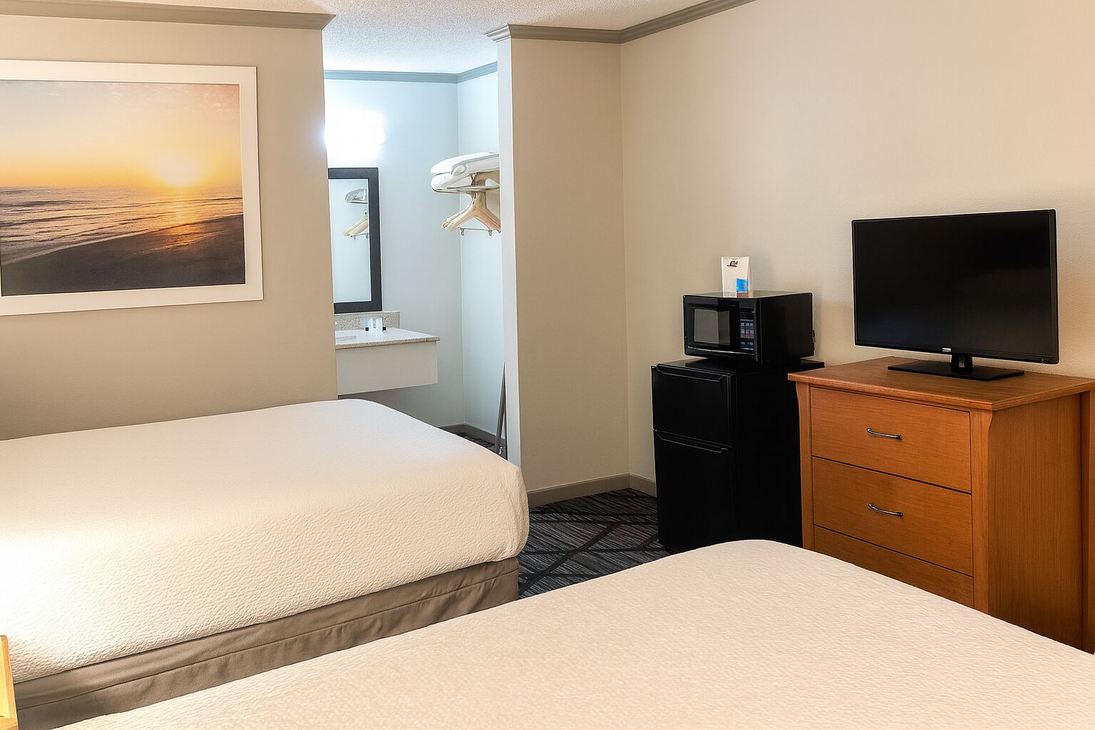Una habitación de hotel con dos camas, televisión, microondas y refrigerador pequeño.