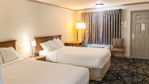 A hotel room with two beds, a chair, a lamp, and a curtain. - Best Inn of Manning (Manning)