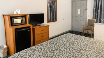 A hotel room with a bed, a television, a refrigerator, a wooden dresser, and a chair.