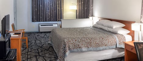 Una habitación de hotel con una cama, un escritorio con computadora, un televisor y una lámpara.