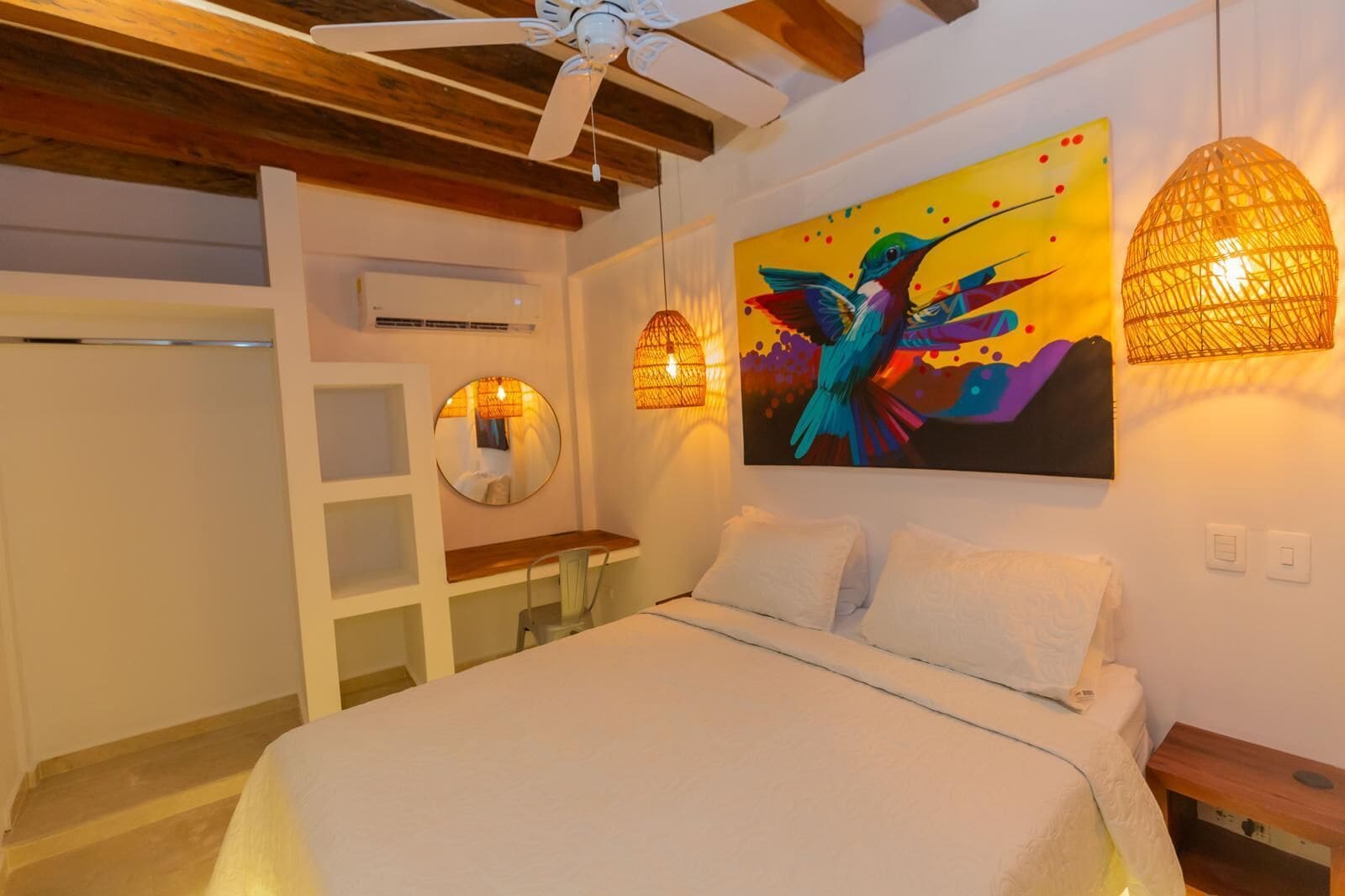 A bedroom with a bed, a ceiling fan, a painting, and two wall-mounted lamps.