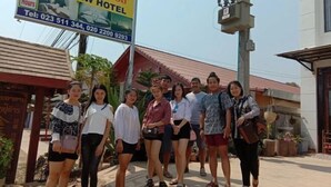 Un groupe de personnes se tient devant une enseigne d’hôtel sur laquelle figurent les coordonnées.