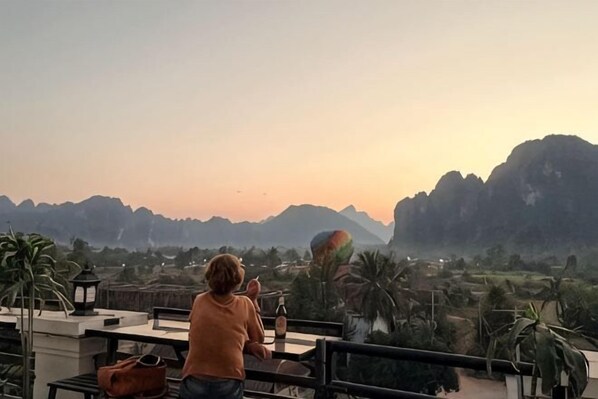 Une personne se trouve sur une terrasse en toit, d’où l’on peut admirer des montagnes et des palmiers.