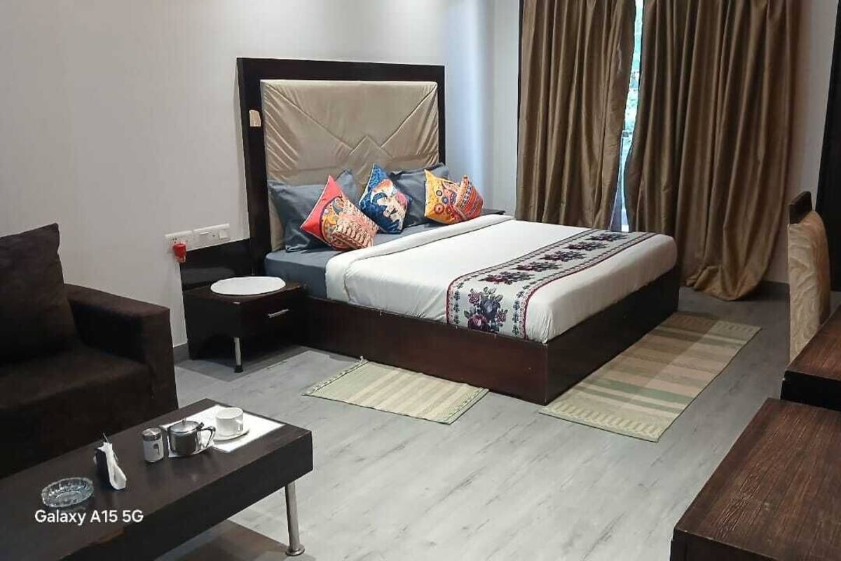 A hotel room with a bed, bedside table, and a small table with a teapot and cups.