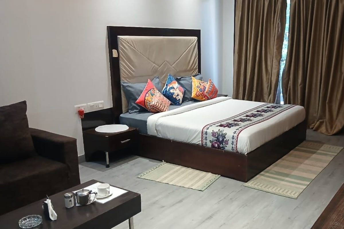 Een hotelkamer met een bed, nachtkastje en een tafeltje met waterkoker en kopjes.
