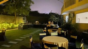 An outdoor dining area with tables and chairs, surrounded by greenery and a building with a balcony. - Hotel Amazone Residency DLF Phase 3  (Gurugram)