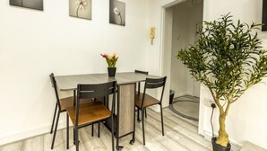 A dining area with a table and chairs, a potted plant, and wall-mounted artwork. - Cozy Flat Near Hyde Park! (Greater London)