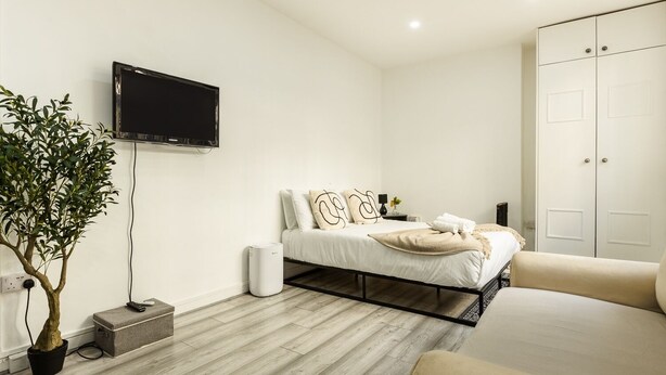 A modern bedroom with a bed, bedside table, and a TV mounted on the wall. - Cozy Flat Near Hyde Park! (Greater London)