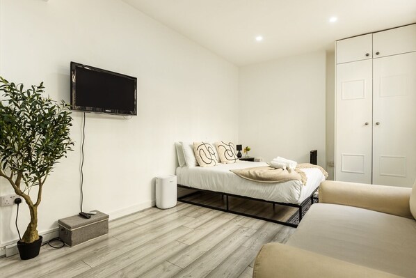 A modern bedroom with a bed, bedside table, and a TV mounted on the wall. - Cozy Flat Near Hyde Park! (Greater London)