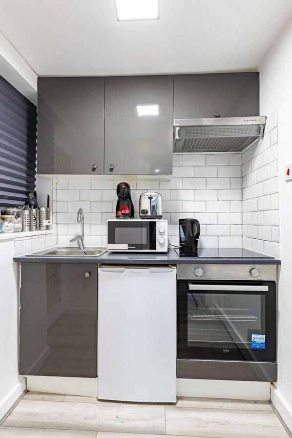 Eine kompakte Küche mit Mikrowelle, Toaster, Kaffeemaschine und einem kleinen Kühlschrank.