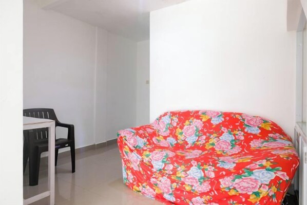 Una habitación con un sofá floral rojo, una mesita con una silla y una pared blanca.