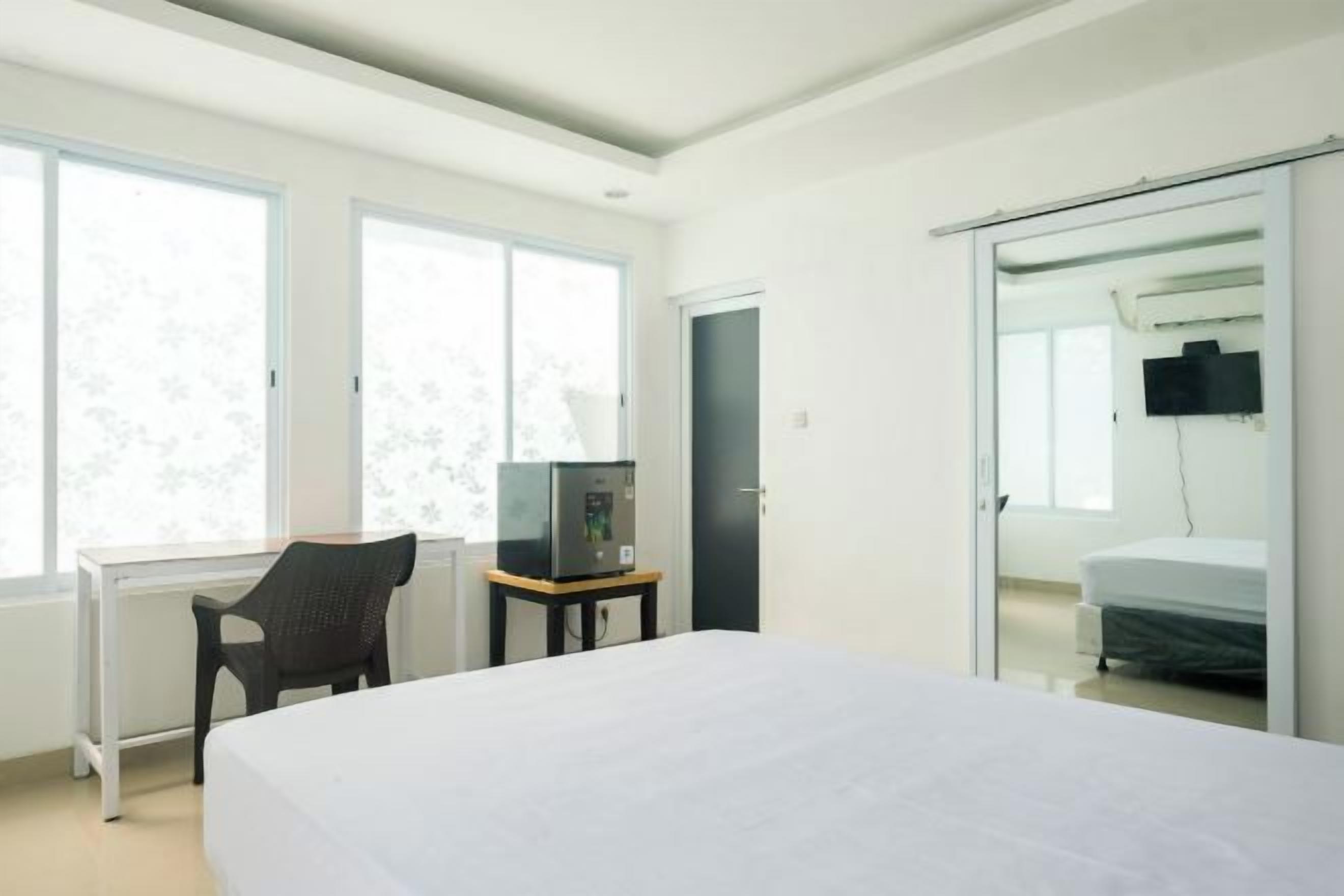 A modern hotel room with a large bed, a desk with a chair, a television, and a sliding door leading to a bathroom.