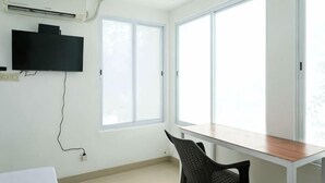 Huoneessa on työpöytä, tuoli, seinälle asennettu televisio ja suuret ikkunat.
