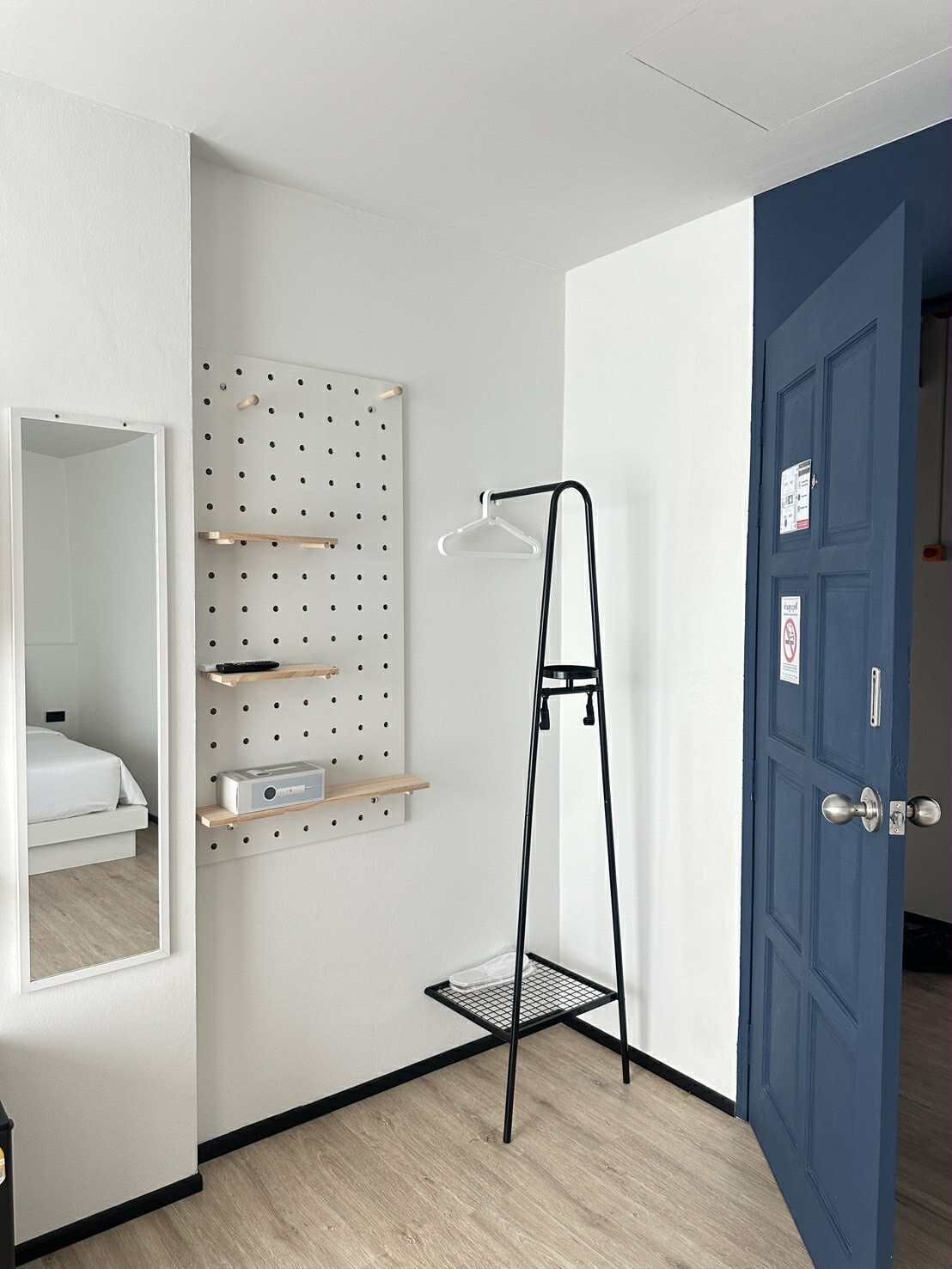 A room with a pegboard wall, a black metal floor lamp, a blue door, and a white bed.
