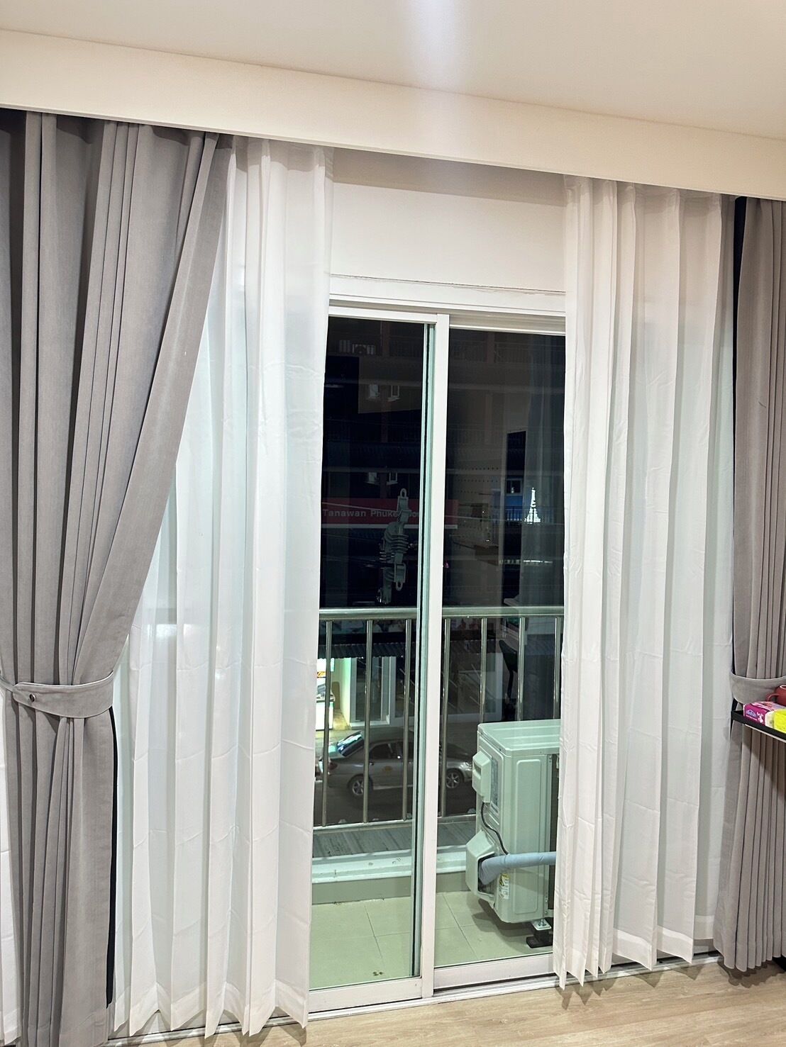 A room with a sliding glass door, white curtains, and a view of a building outside.