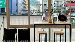Una habitación con un ventanal grande, dos sillas negras, una mesita y una planta en maceta.