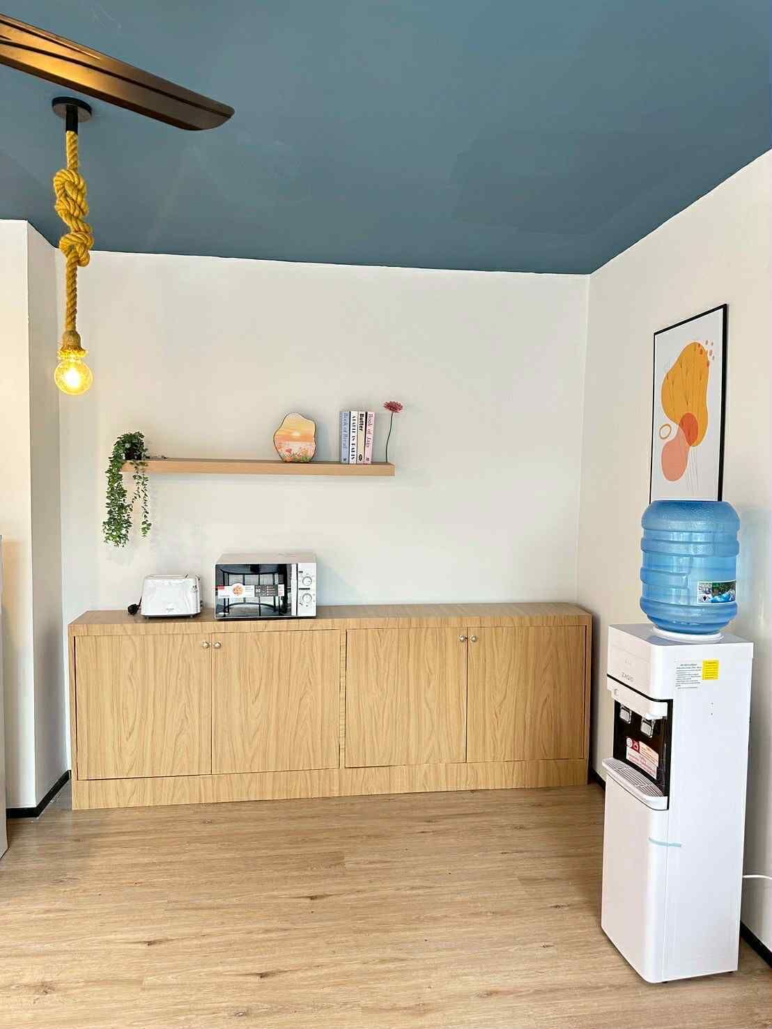 A modern kitchen with wooden cabinets, a built-in microwave, a water dispenser, and a hanging light fixture.