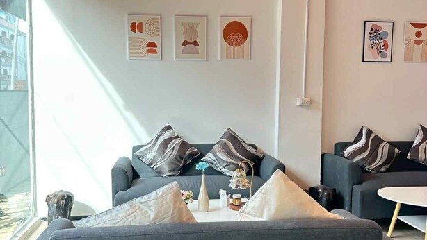 Una sala moderna con un sofá gris, una mesa de centro y una mesita auxiliar. Hay obras de arte abstracto en la pared y una ventana que proporciona luz natural.