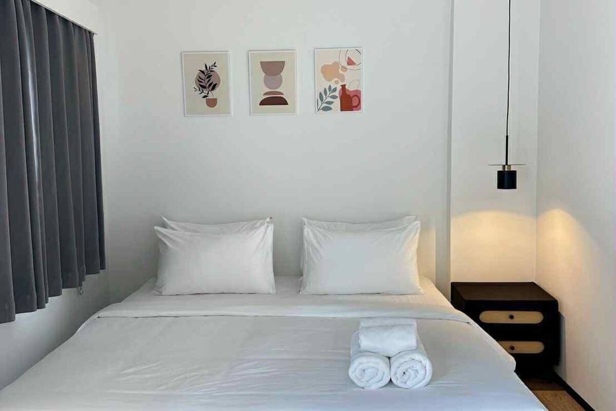 Ein modernes Hotelzimmer mit einem großen Bett, weißer Bettwäsche, einem Nachttisch und drei Wandbildern.