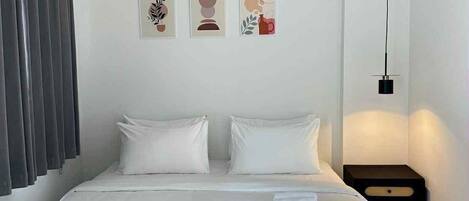 A modern hotel room with a large bed, white bedding, a nightstand, and three wall art pieces.