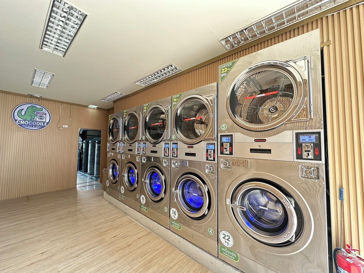 A laundromat with multiple washing machines and dryers, a wooden floor, and a sign for 'Crocodile Wash & Dry'.
