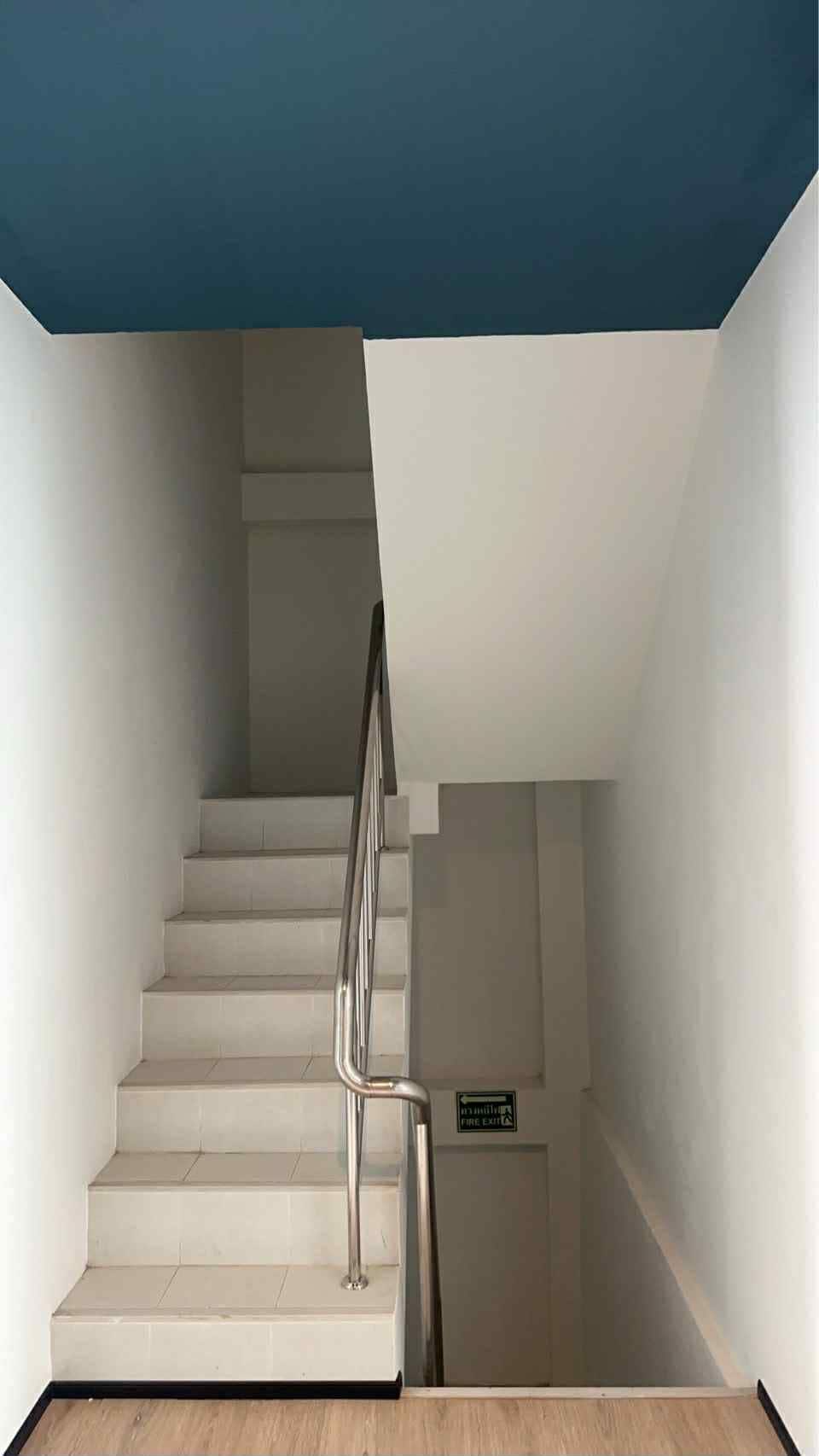 A staircase with a metal handrail, white walls, and a blue ceiling.