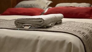 Ein ordentlich bezogenes Bett mit einem gefalteten weißen Handtuch, roten Kissen und einem hölzernen Kopfteil.