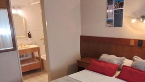 Ein Hotelzimmer mit Bett, Nachttisch, Spiegel und einem durch eine offene Tür einsehbaren Badezimmer.