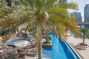 A swimming pool with palm trees, lounge chairs, and a view of the city skyline. - Park Island Residences by CEG Group (Dubai)