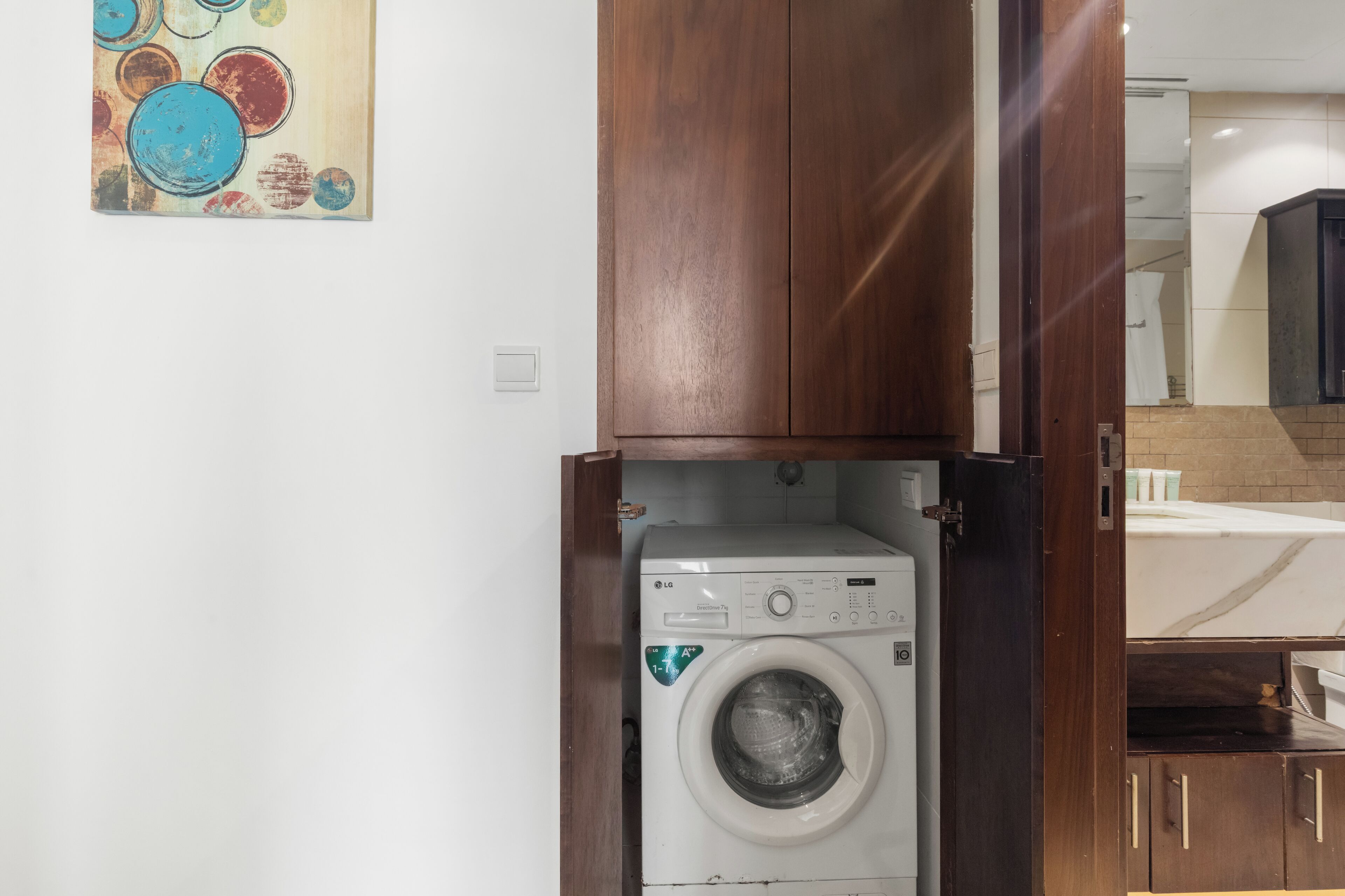 A compact laundry room with a front-loading washing machine, wooden cabinets, and a tiled backsplash.
