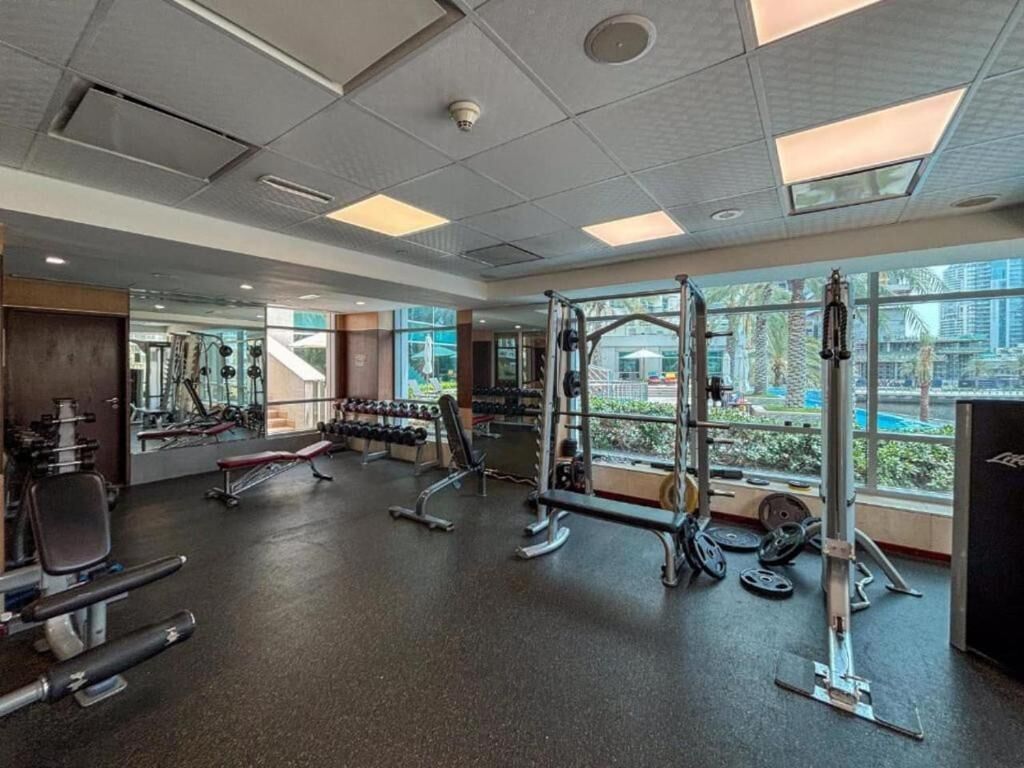Une salle de sport équipée de divers appareils d’exercice, dotée de grandes fenêtres et offrant une vue sur la ville.
