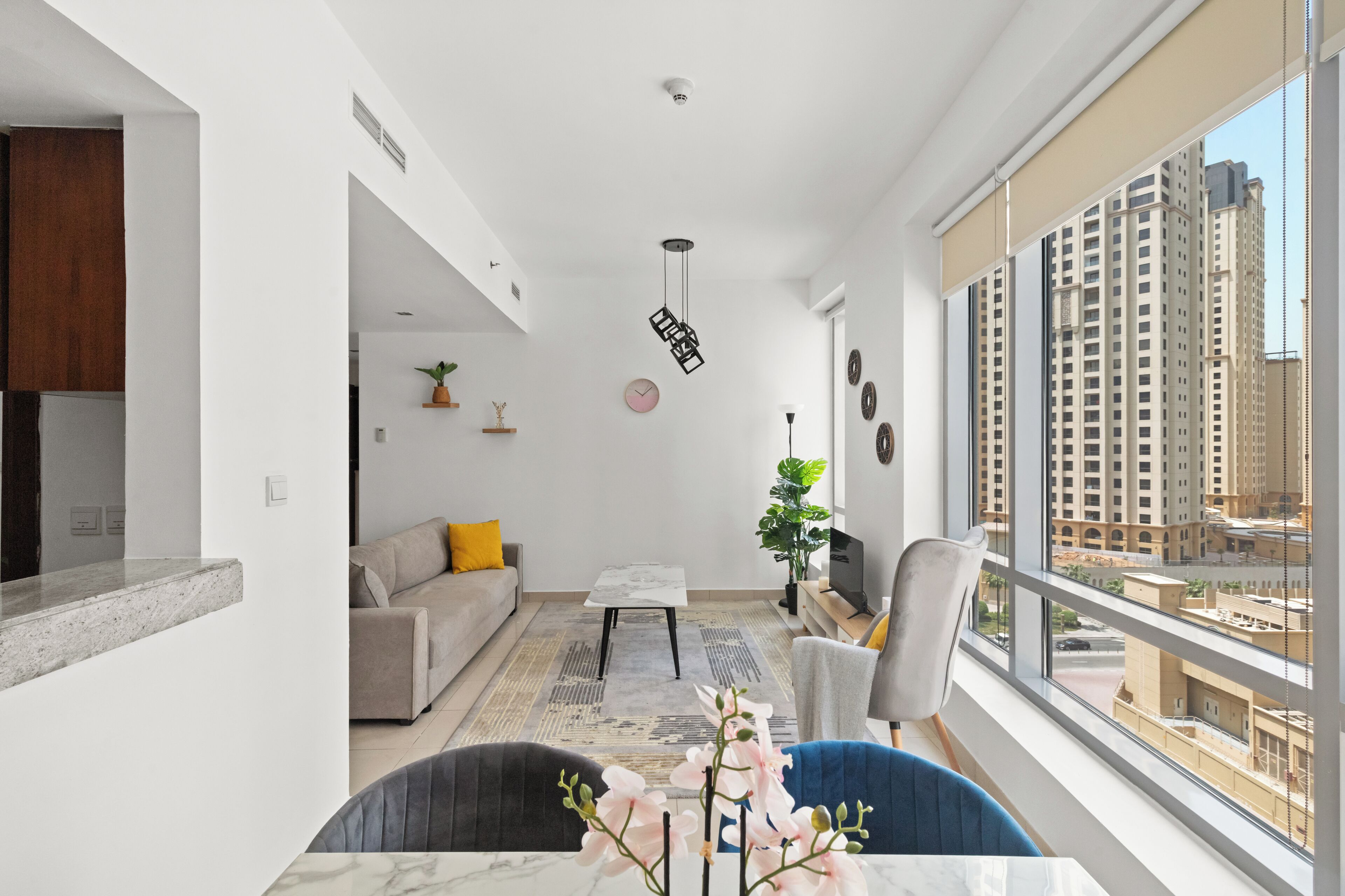 A modern living room with a sofa, coffee table, and a view of tall buildings through large windows.