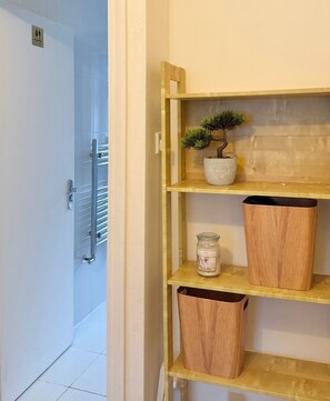 A bathroom with a toilet, a shelf with a potted plant, a candle, and a trash bin. - Elysian Nights  (London)