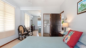A bedroom with a bed, a chair, a desk, and a door leading to a bathroom.