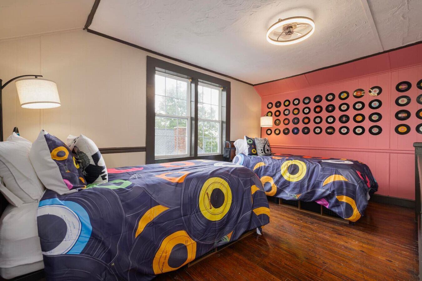 A room with two beds, a wall of vinyl records, and a large window.