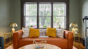 Ein gemütliches Wohnzimmer mit einer braunen Ledersofa, zwei gelben Kissen und einem runden Couchtisch. Auf jeder Seite des Sofas stehen jeweils zwei Stehlampen.