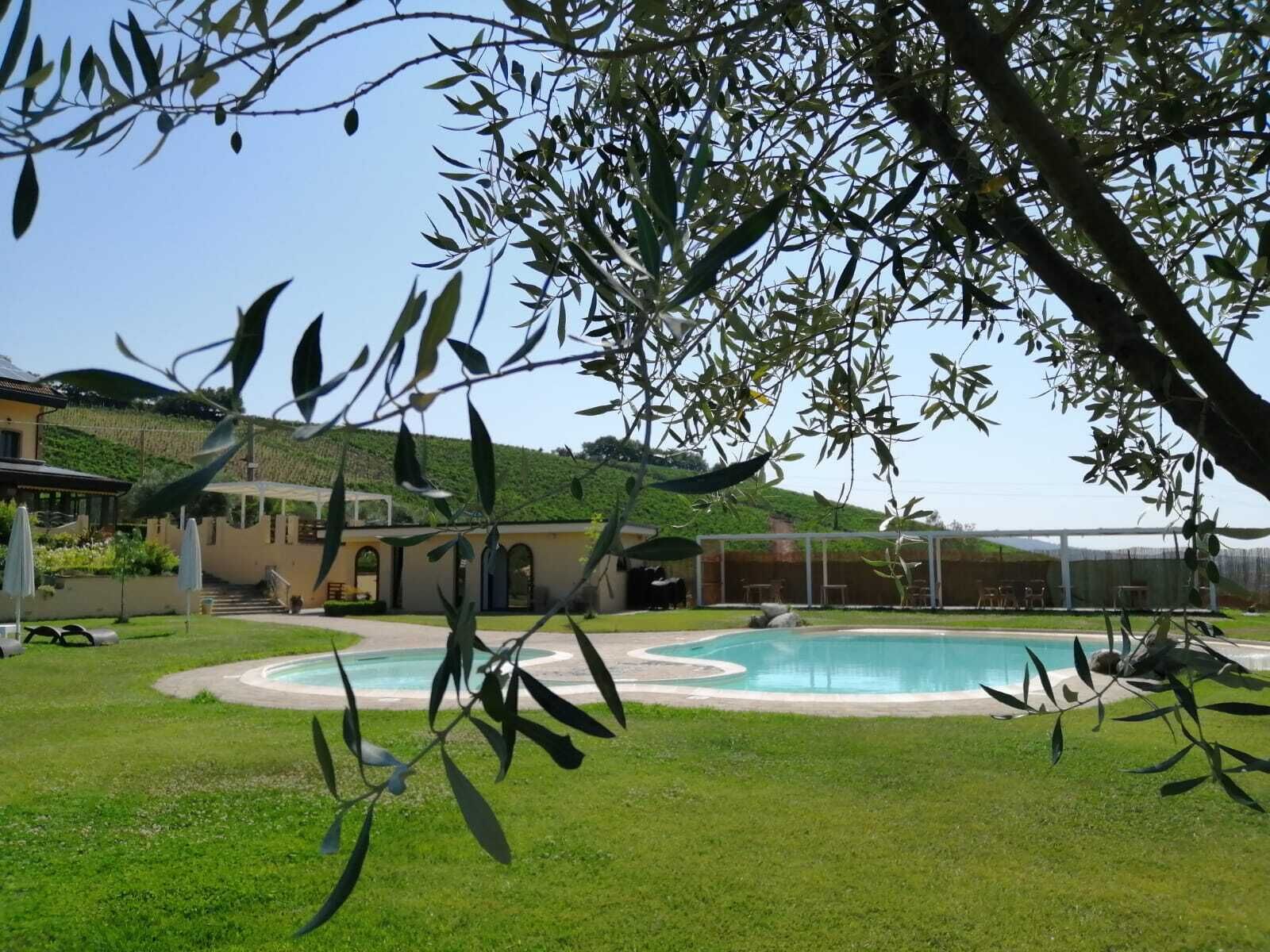Zona de piscina con una casa al fondo, rodeada de vegetación y colinas.