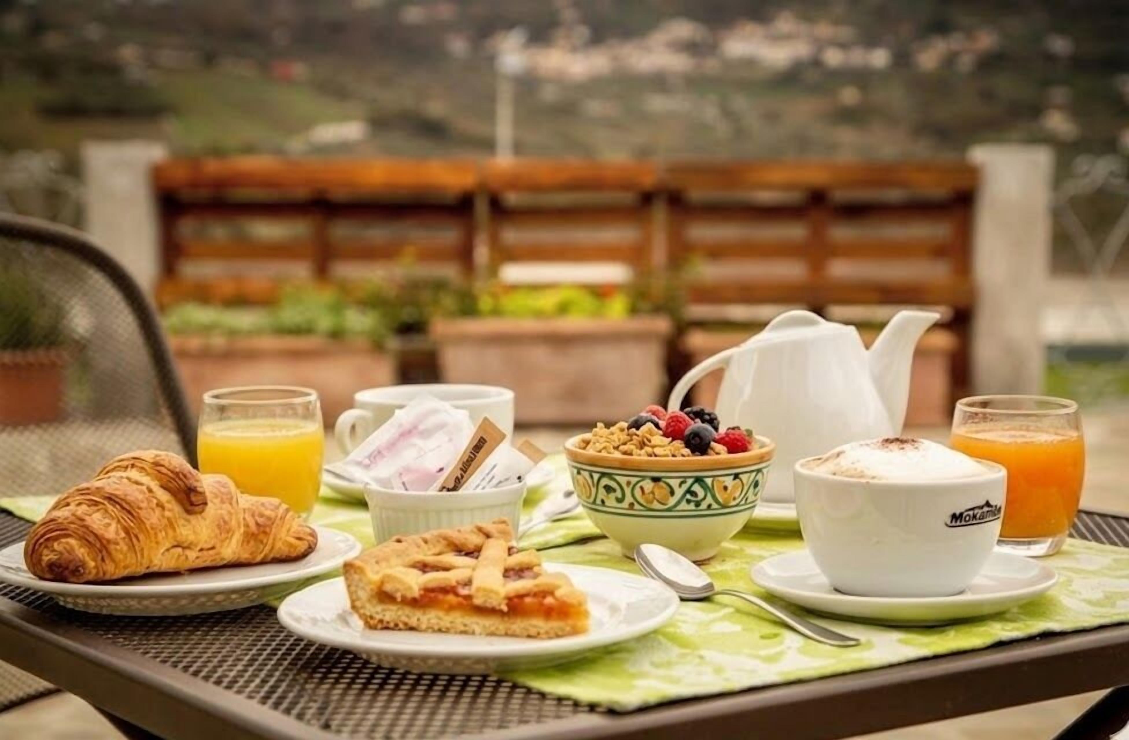 Une table avec des aliments pour le petit-déjeuner, notamment des croissants, une tarte, un saladier de fruits, une tasse de café et un verre de jus d’orange.