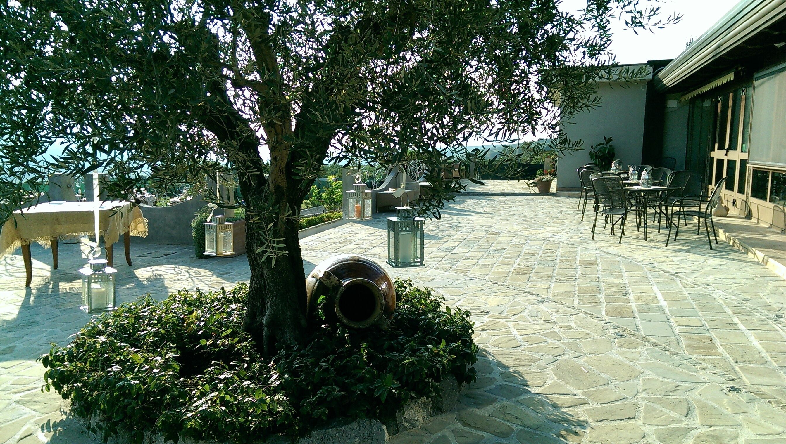 An outdoor patio with stone flooring, tables, chairs, and a tree.