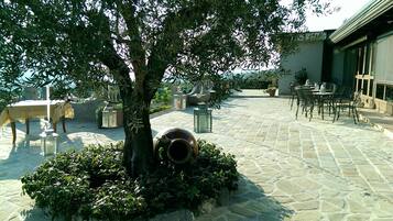 An outdoor patio with stone flooring, tables, chairs, and a tree.