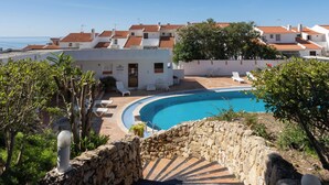 A pool area with a stone wall, a staircase, and a view of white buildings with red roofs. - Bem Parece by Umbral (Albufeira)