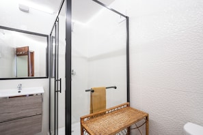 A bathroom with a glass shower enclosure, a wooden bench, a white sink, and a towel rack. - Bem Parece by Umbral (Albufeira)