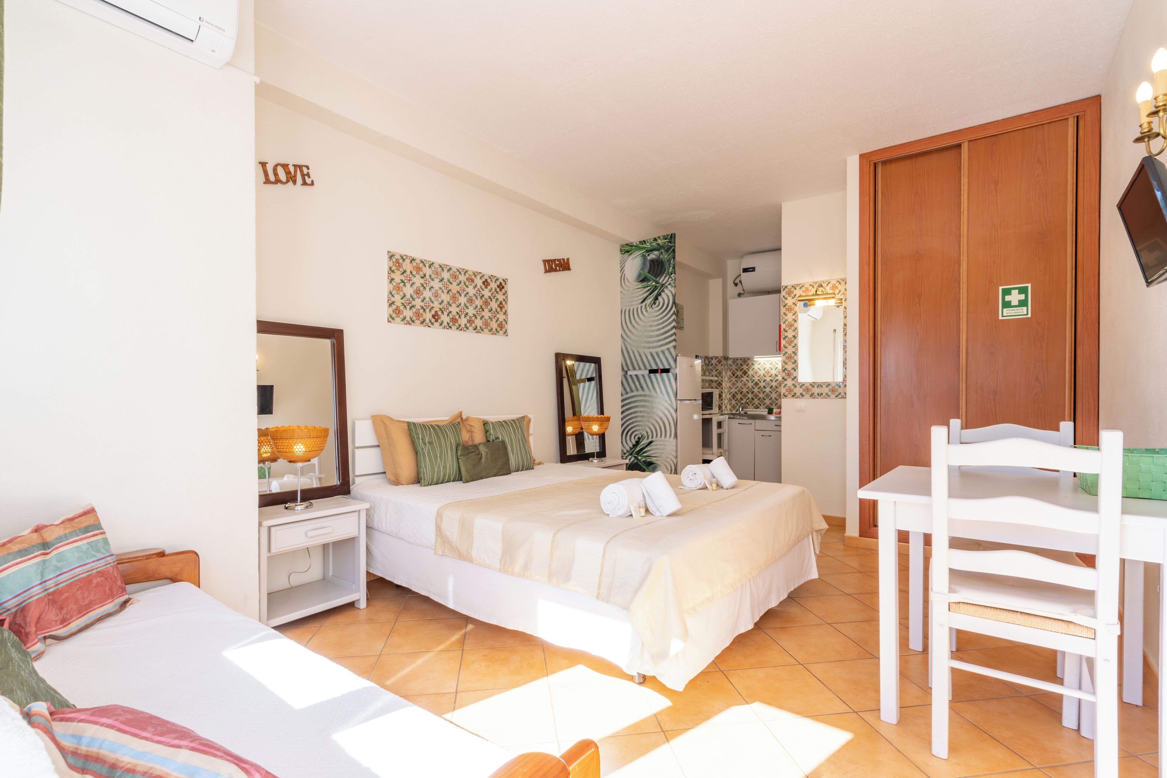 A hotel room with a bed, bedside table, chair, and a small kitchenette.