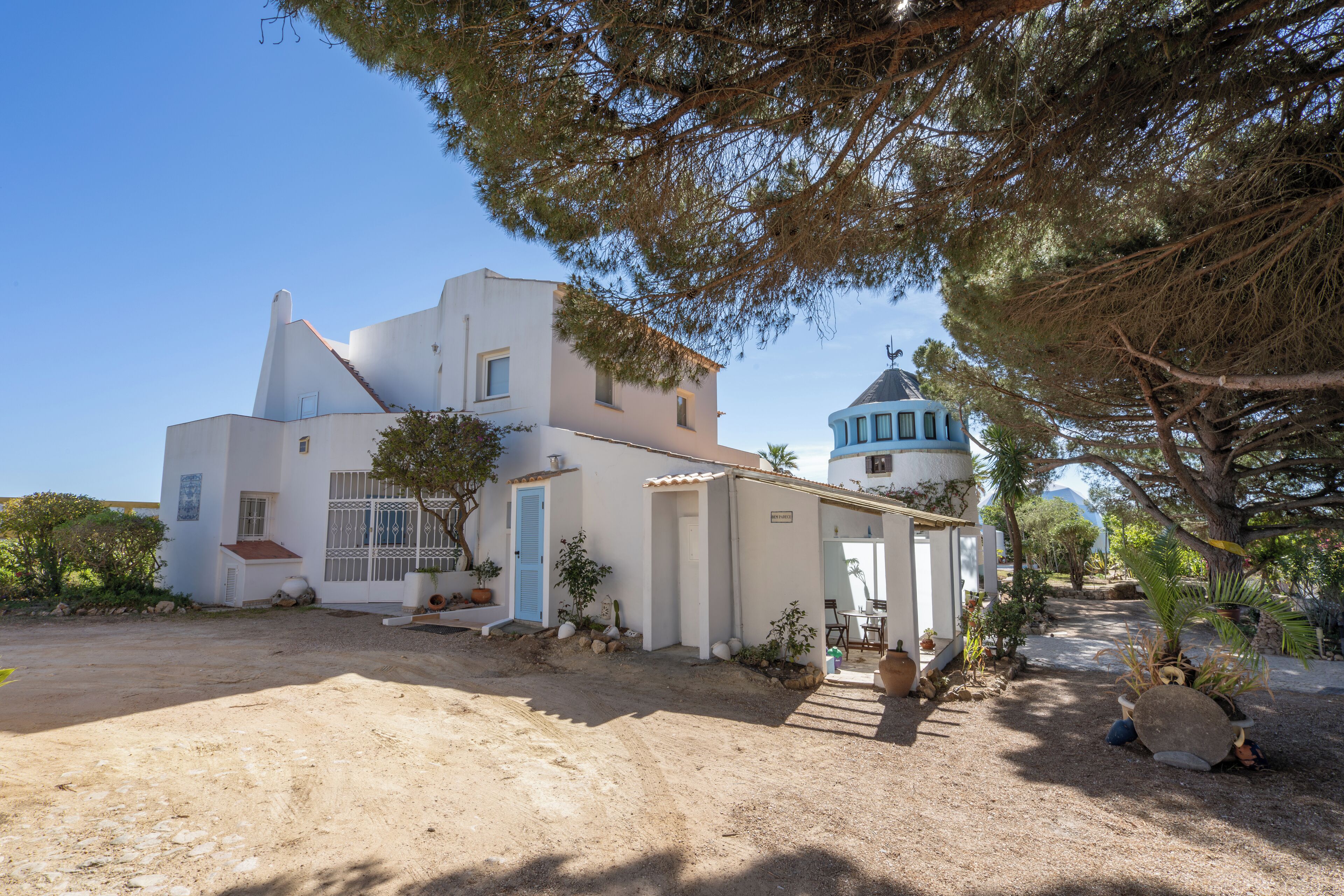 Un bâtiment blanc avec une porte bleue et une petite structure adjacente surmontée d’un toit bleu.