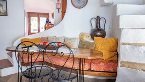 A cozy room with a stone floor, a wooden ceiling, a sofa with cushions, a table with chairs, and a wall clock. - Bem Parece by Umbral (Albufeira)