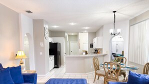 A modern living room with blue sofas, a coffee table, and a dining area with a glass table and chairs. - SD2216MC – Golf-side 5-Bed Villa with Private Pool (Haines City)