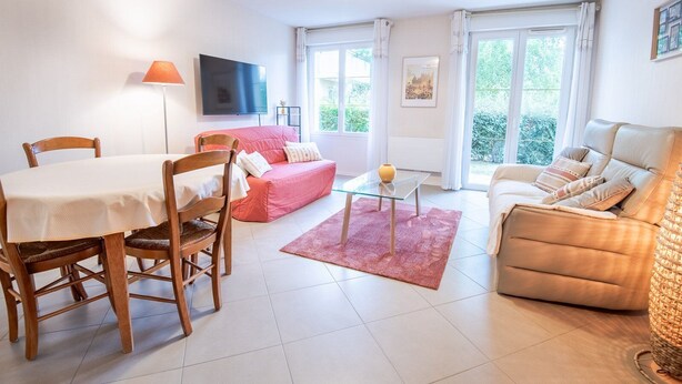 Una sala de estar moderna con una mesa de comedor, dos sofás, un televisor y ventanas amplias.