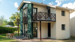 Une maison à deux étages dotée d’un balcon, d’un espace salon extérieur et d’un jardin.