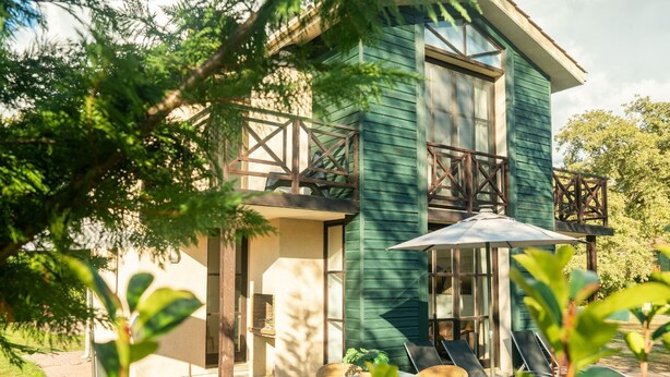 Une maison à deux étages avec un balcon, une terrasse avec une table et des chaises, et un grand parasol.